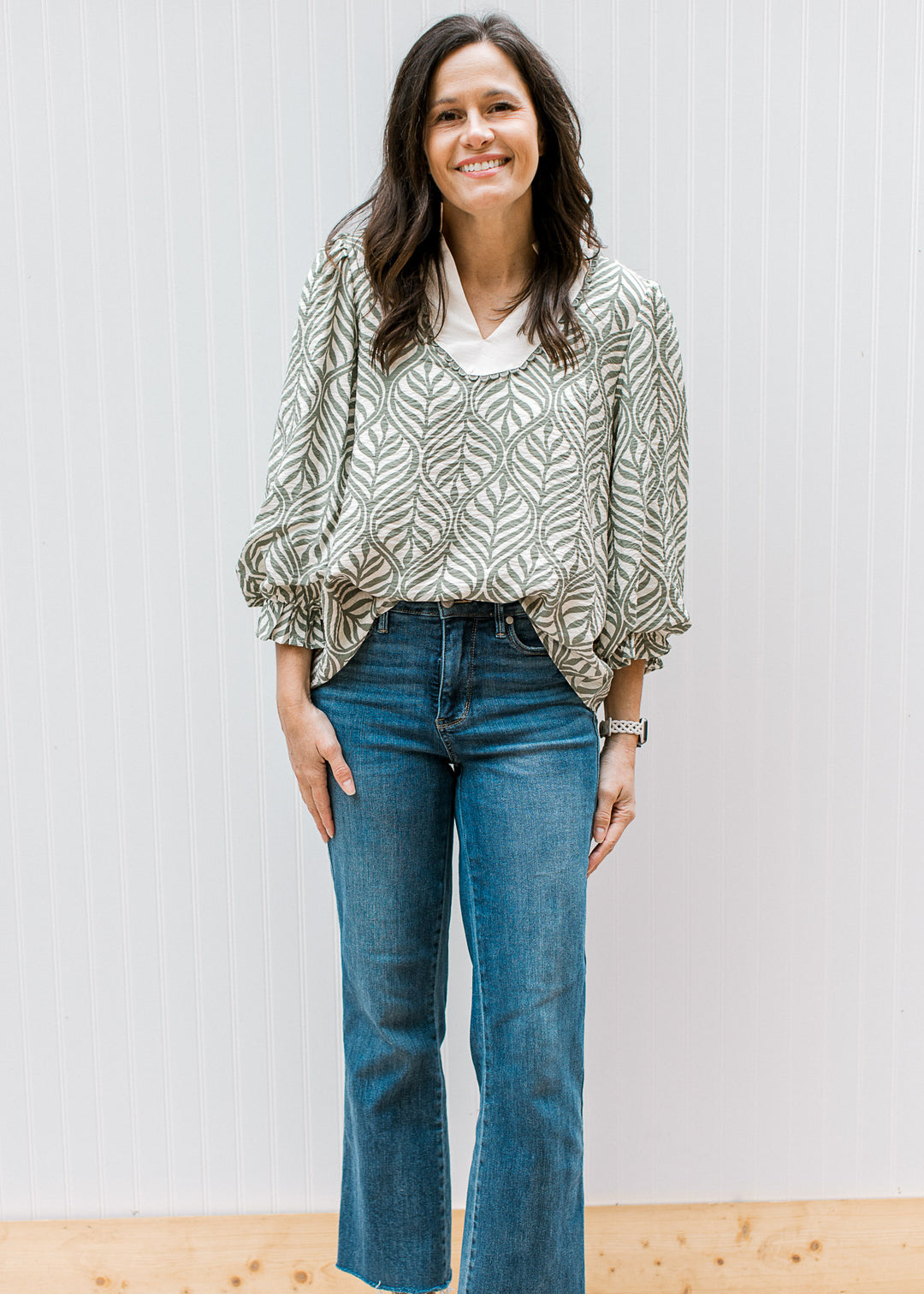 Model wearing jeans and a cream top with olive leaf pattern, cream v-neck and 3/4 poet sleeves. 