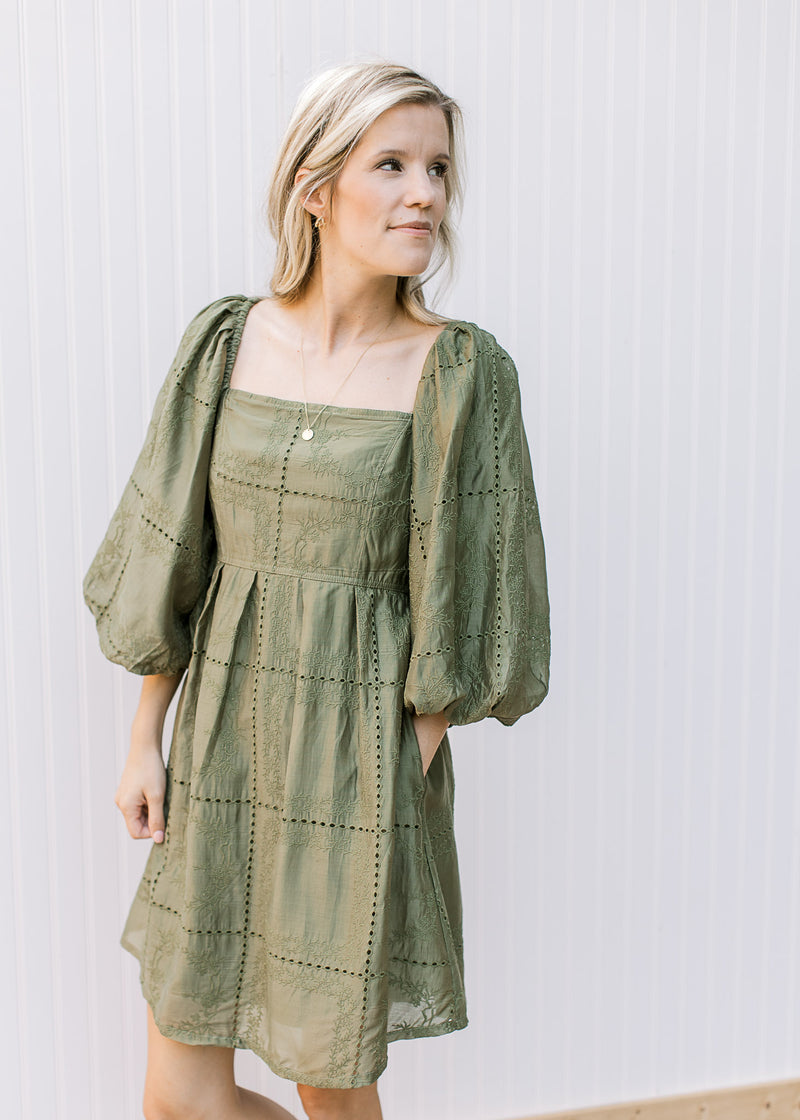 Model wearing an olive dress with eyelet detail, pockets, square neck and 3/4 sleeves.