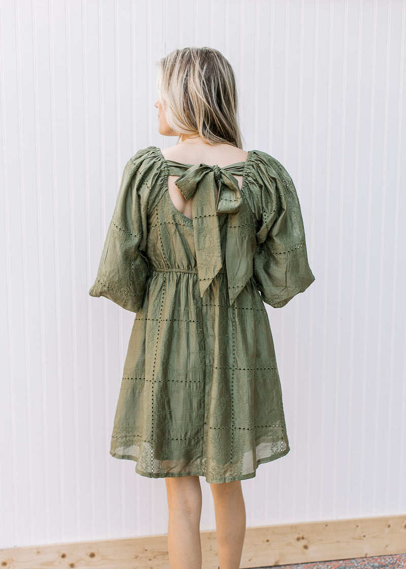 Back view of Model wearing an olive dress with a square neck with a tie and 3/4 bubble sleeves.