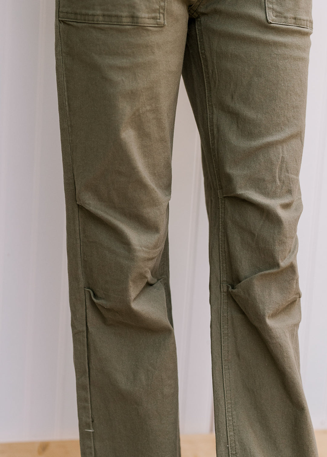 Close up of straight leg fit design and patch front pockets on a model in olive green denim. 