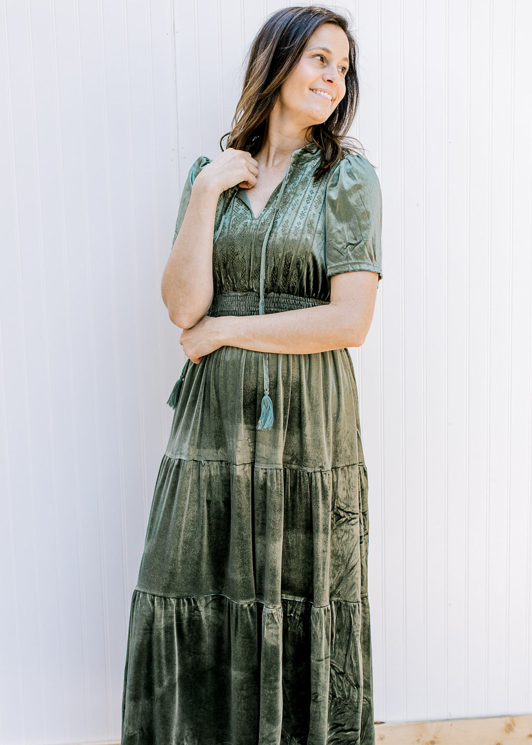 Model wearing a velvet olive dress with tiered skirt, v-neck with a tie and short sleeves. 
