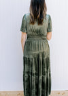 Back view of Model wearing an olive dress with tiered skirt, v-neck with a tie and short sleeves.