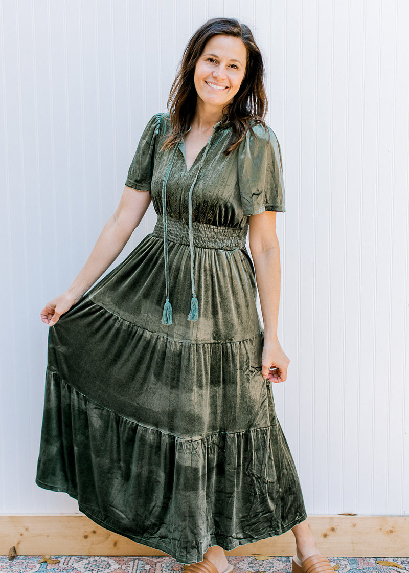 Model wearing a velvet olive dress with elastic wasit, v-neck with a tie and short sleeves. 