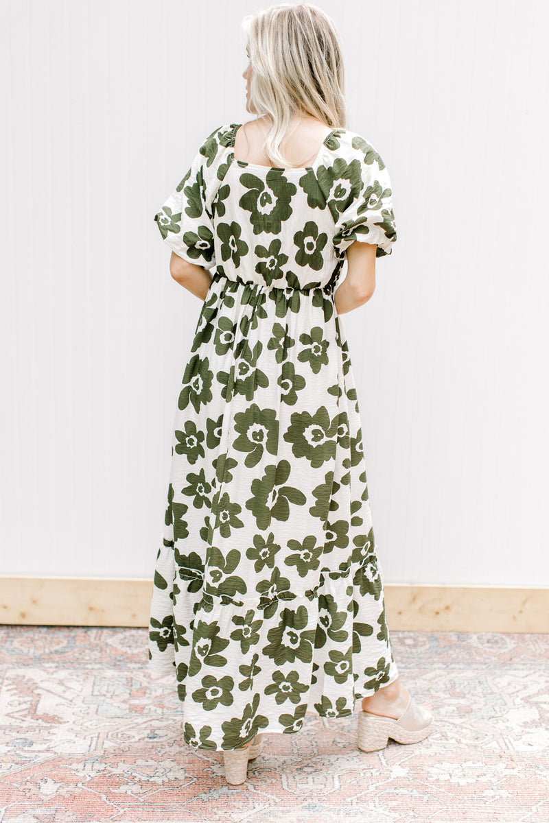 Back view of Model wearing a cream dress with olive flowers, square neck and bubble short sleeves.