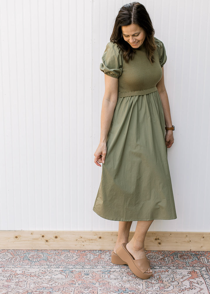 Model wearing an olive midi with a ribbed bodice, mock neck and short puff sleeves.