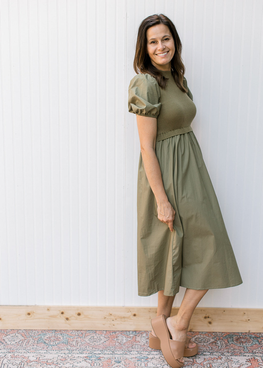 Model wearing an olive dress with a ribbed bodice, mock neck and short puff sleeves.