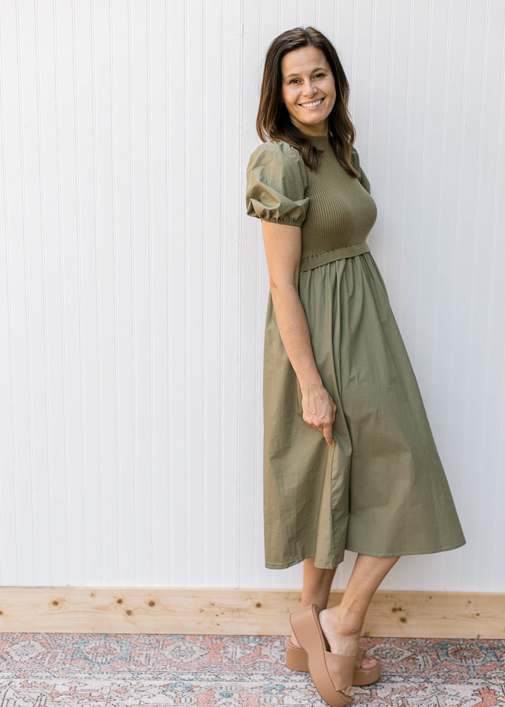 Model wearing an olive dress with a ribbed bodice, mock neck and short puff sleeves.