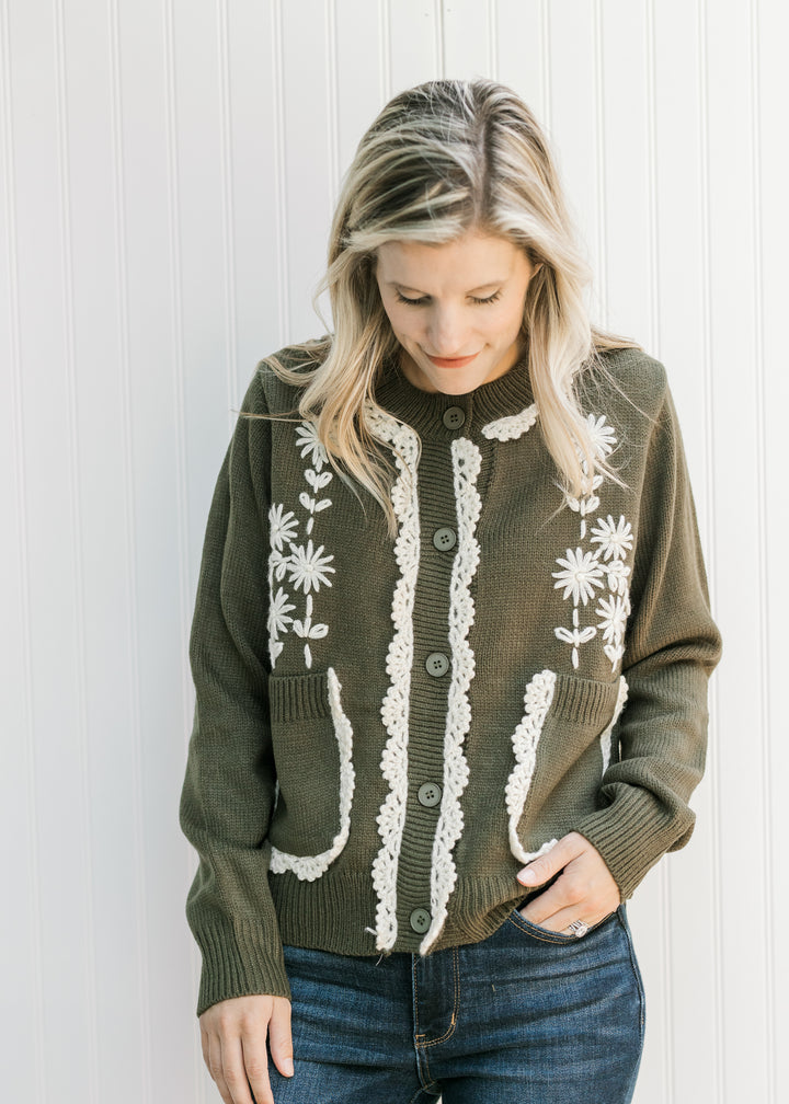 Model wearing an olive cardigan with cream embroidered lace, patch pockets and long sleeves. 