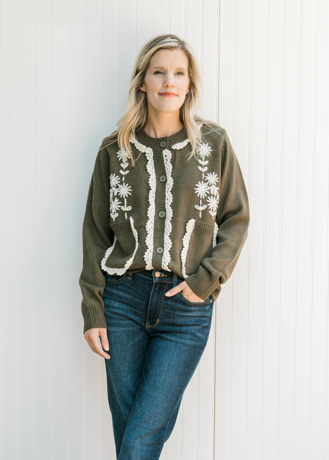Model wearing an olive button down cardigan with cream embroidered lace and long sleeves. 