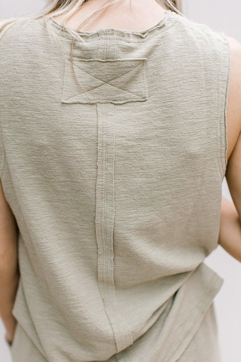 Close up of exposed hem on a light olive sleeveless knit top with matching wide leg bottoms.