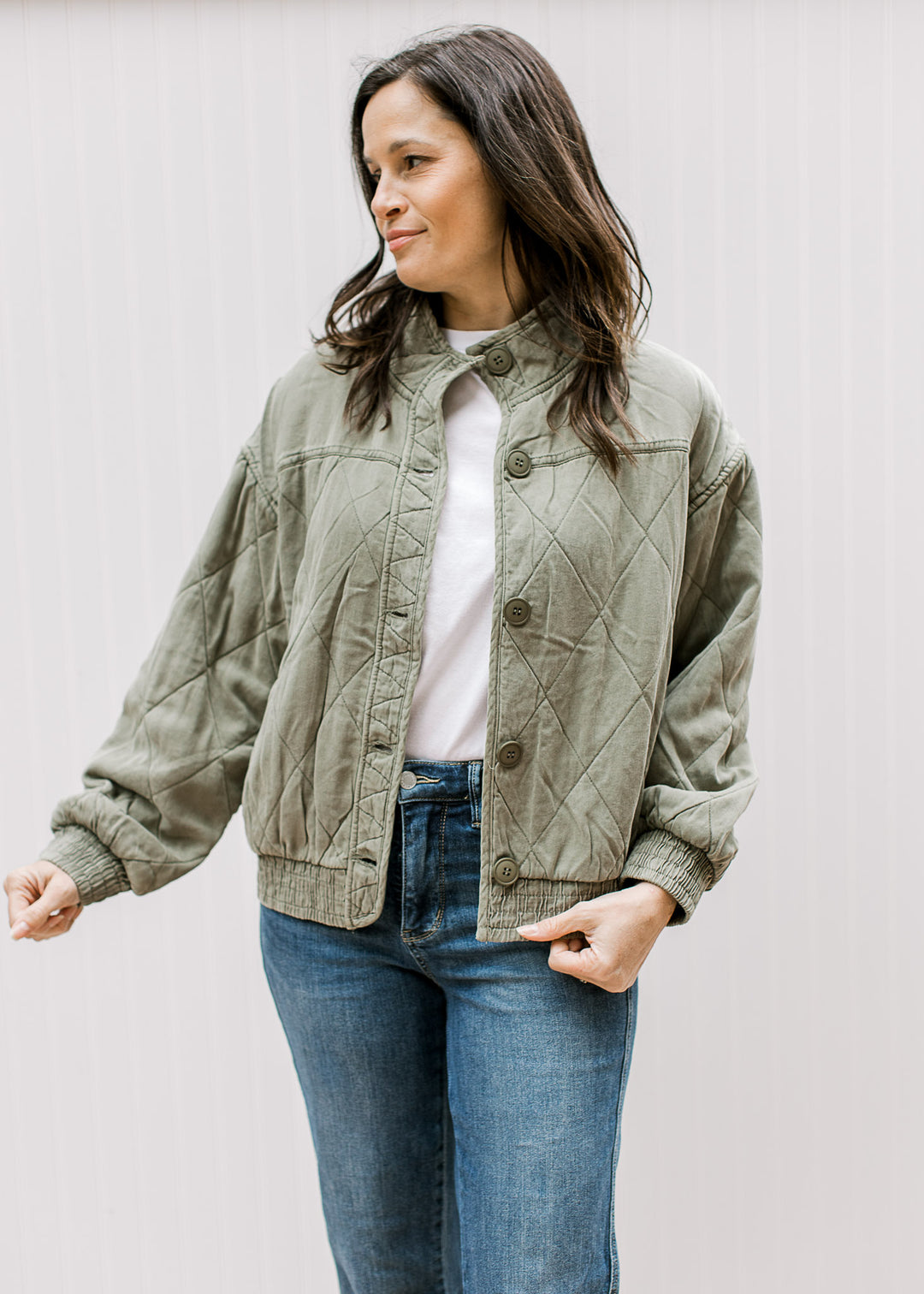 Model wearing an olive quilted jacket with button front and elastic at the hem and long sleeves. 