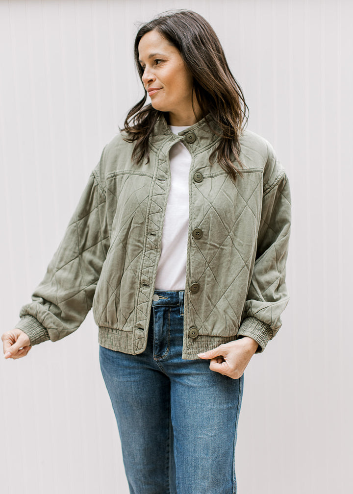 Model wearing an olive quilted jacket with button front and elastic at the hem and long sleeves. 