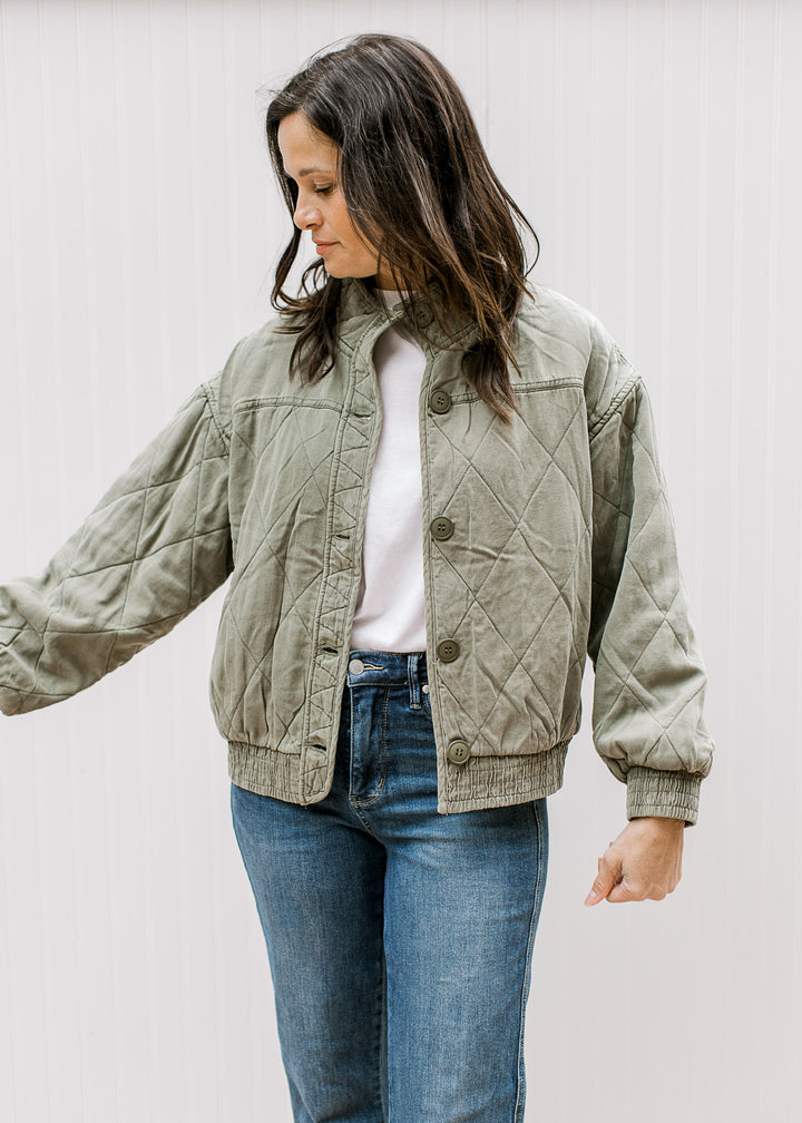 Model wearing jeans and an olive quilted jacket with button front, long sleeves and a mock neck. 