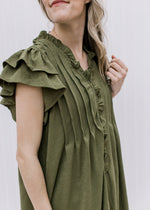 Close up of tiered ruffle short sleeves, pleated bodice and buttons on an olive tunic.