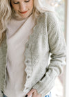 Model wearing a cream top with a soft olive button up long sleeve cardigan with scalloped edging.