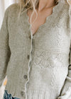 Close up of scalloped edging and buttons on a soft olive cardigan with long sleeves. 