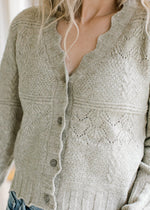 Close up of scalloped edging and buttons on a soft olive cardigan with long sleeves. 