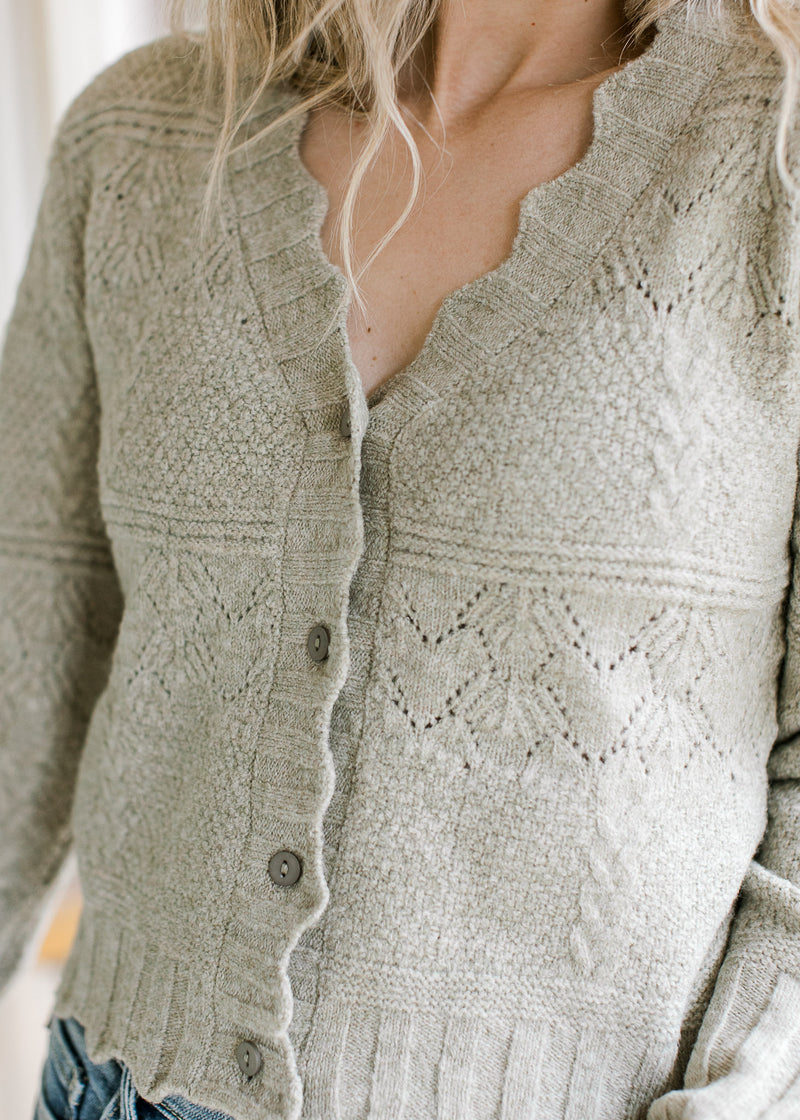 Close up of scalloped edging and buttons on a soft olive cardigan with long sleeves. 