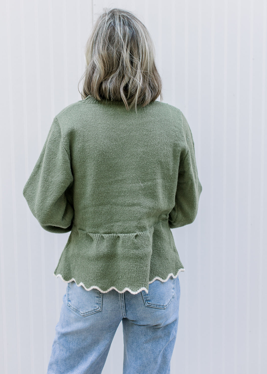 Back view of Model wearing an olive peplum sweater with cream scalloped trim and long sleeves.