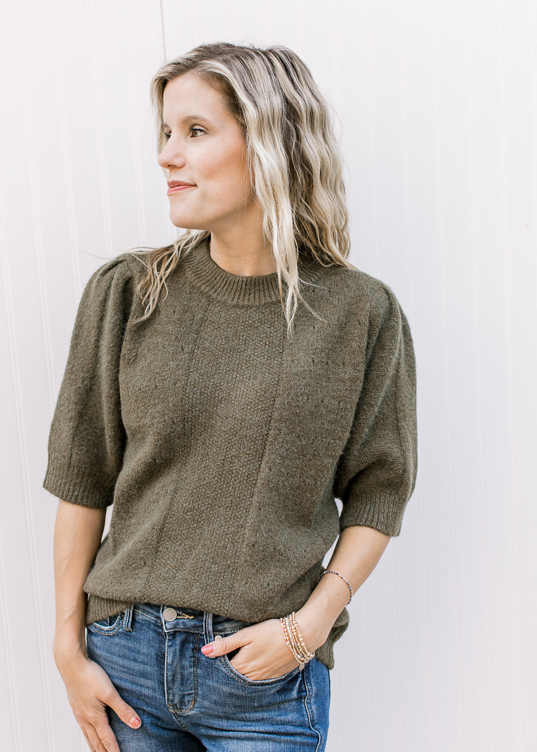 Model wearing an olive short sleeve sweater with subtle texture detail and a round neck.
