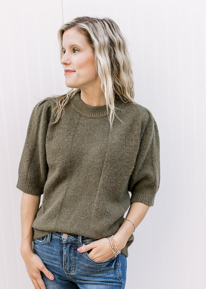 Model wearing an olive short sleeve sweater with subtle texture detail and a round neck.
