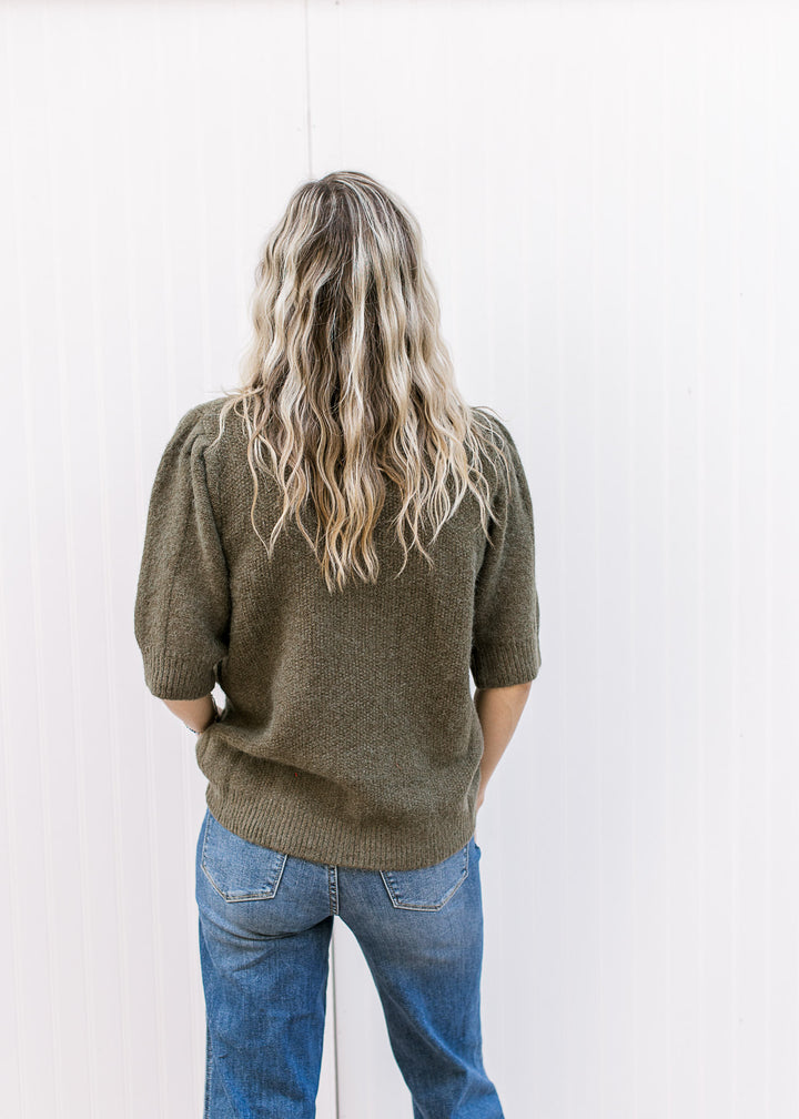 Back view of Model wearing an olive short sleeve sweater with texture detail and a round neck.