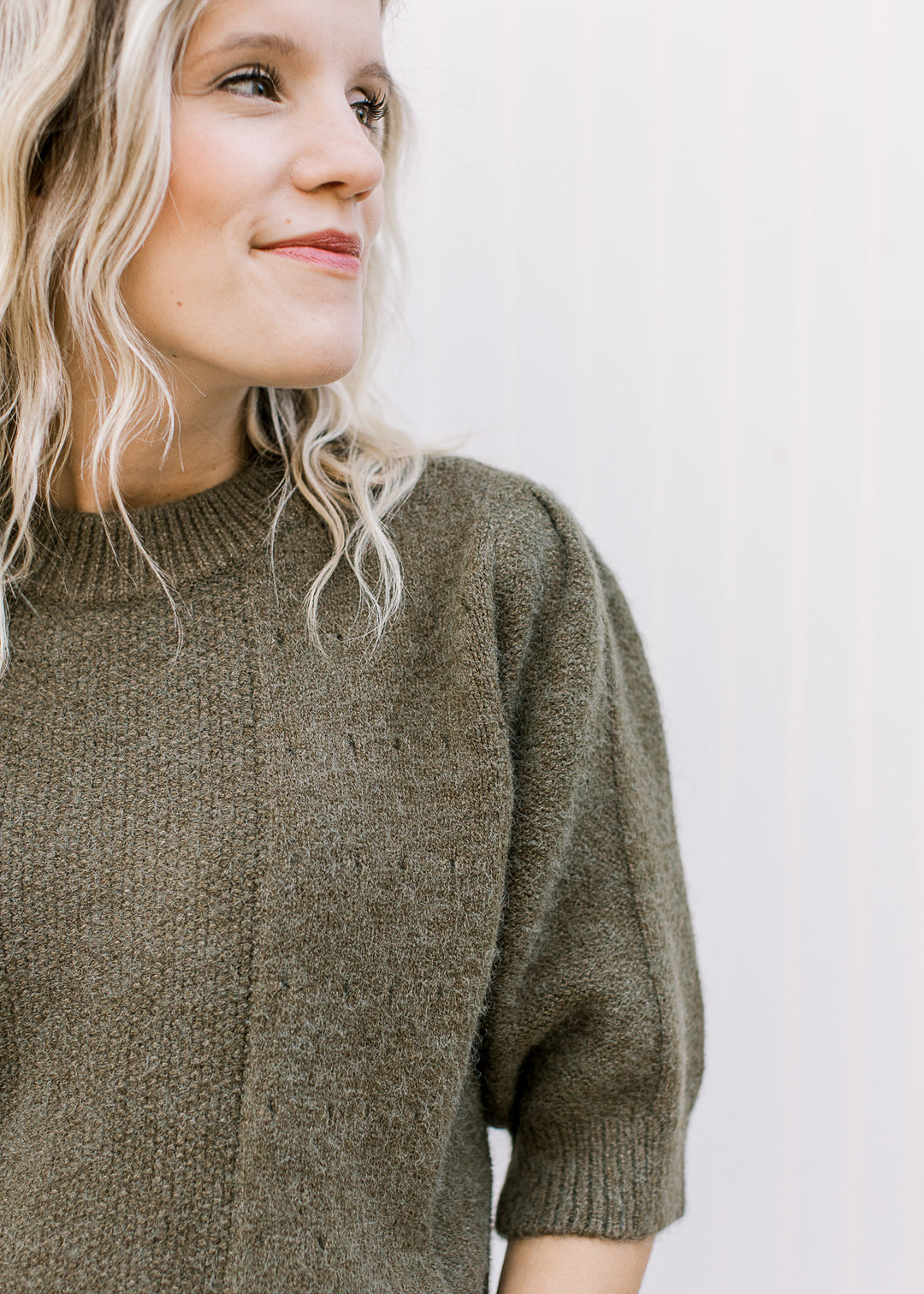 Close up of textured detail and round neck on an olive sweater with short sleeves. 