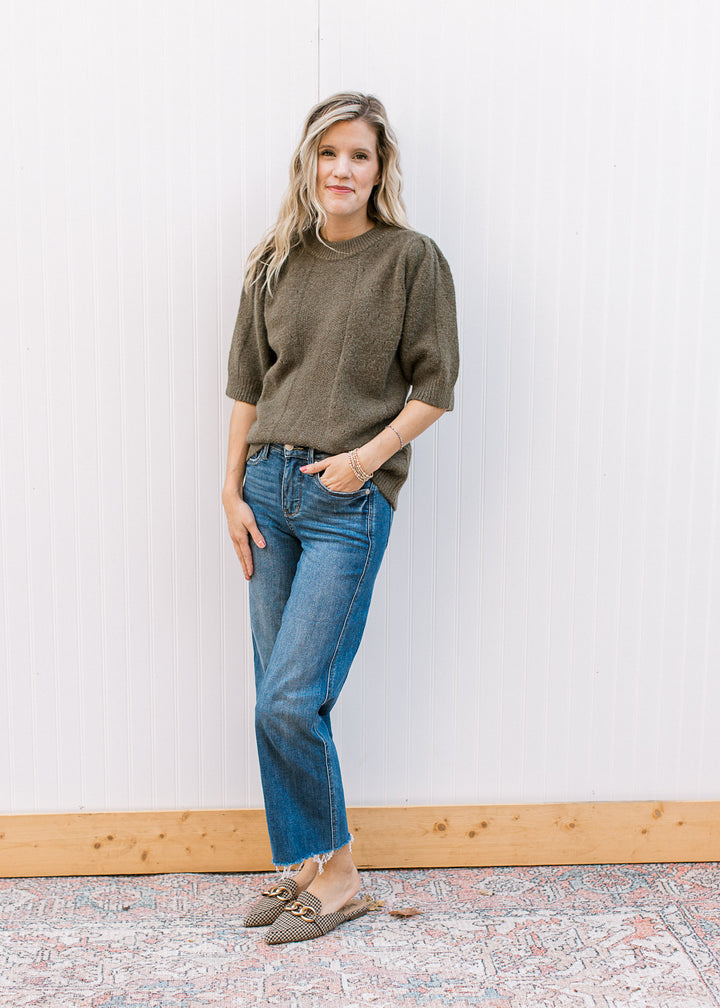 Model wearing jeans and an olive short sleeve sweater with subtle texture detail and a round neck.