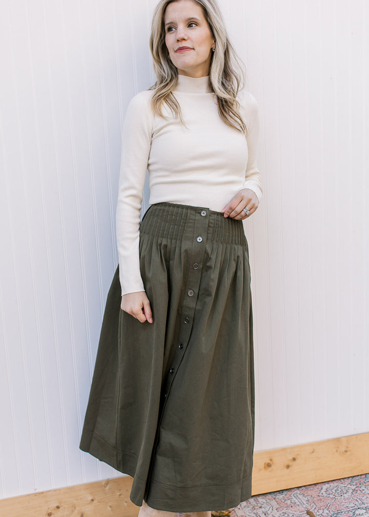 Model wearing an olive midi skirt with pleated detail at waist, elastic back and button down front. 