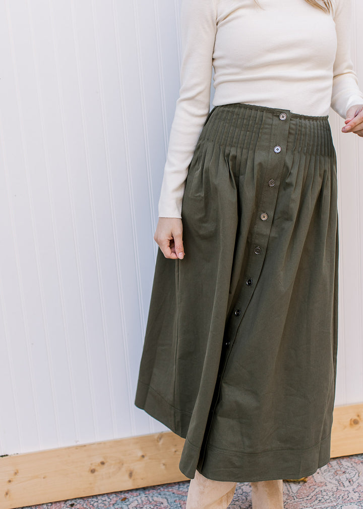 Model wearing an olive skirt with pleated detail at waist, elastic back and button down front. 