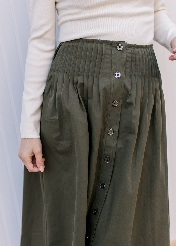 Close up of pleating at waist and button front on a flowy olive midi with pockets. 