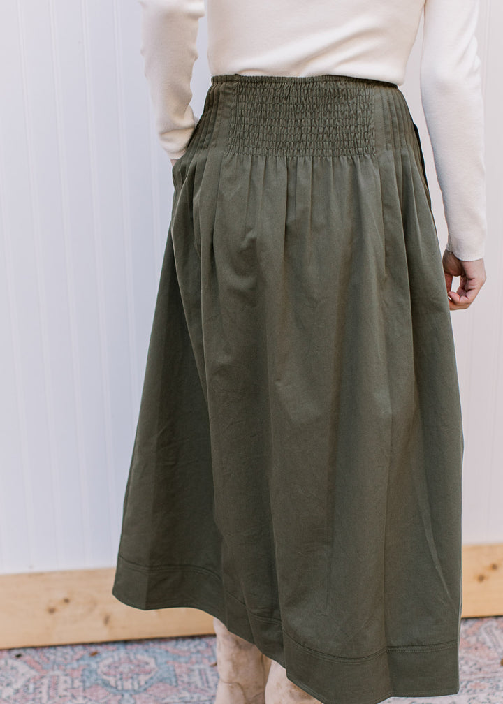 Back view of Model wearing an olive midi skirt with pleated detail at waist and elastic back. 