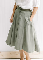 Model wearing an olive midi swing skirt comprised of polyester, with button up closure and pockets. 