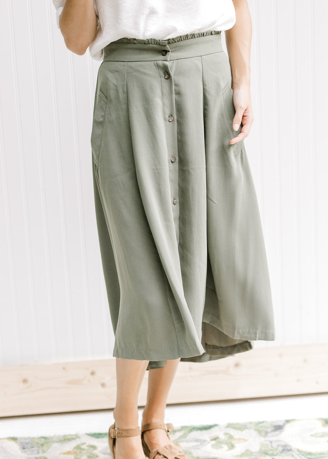 Model wearing sandals with an olive midi swing skirt with button up closure and pockets. 