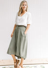 Model wearing an olive midi skirt comprised of polyester, with button up closure and pockets. 