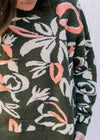 Close up of cream flowers and coral accents on an olive sweater with long sleeves. 