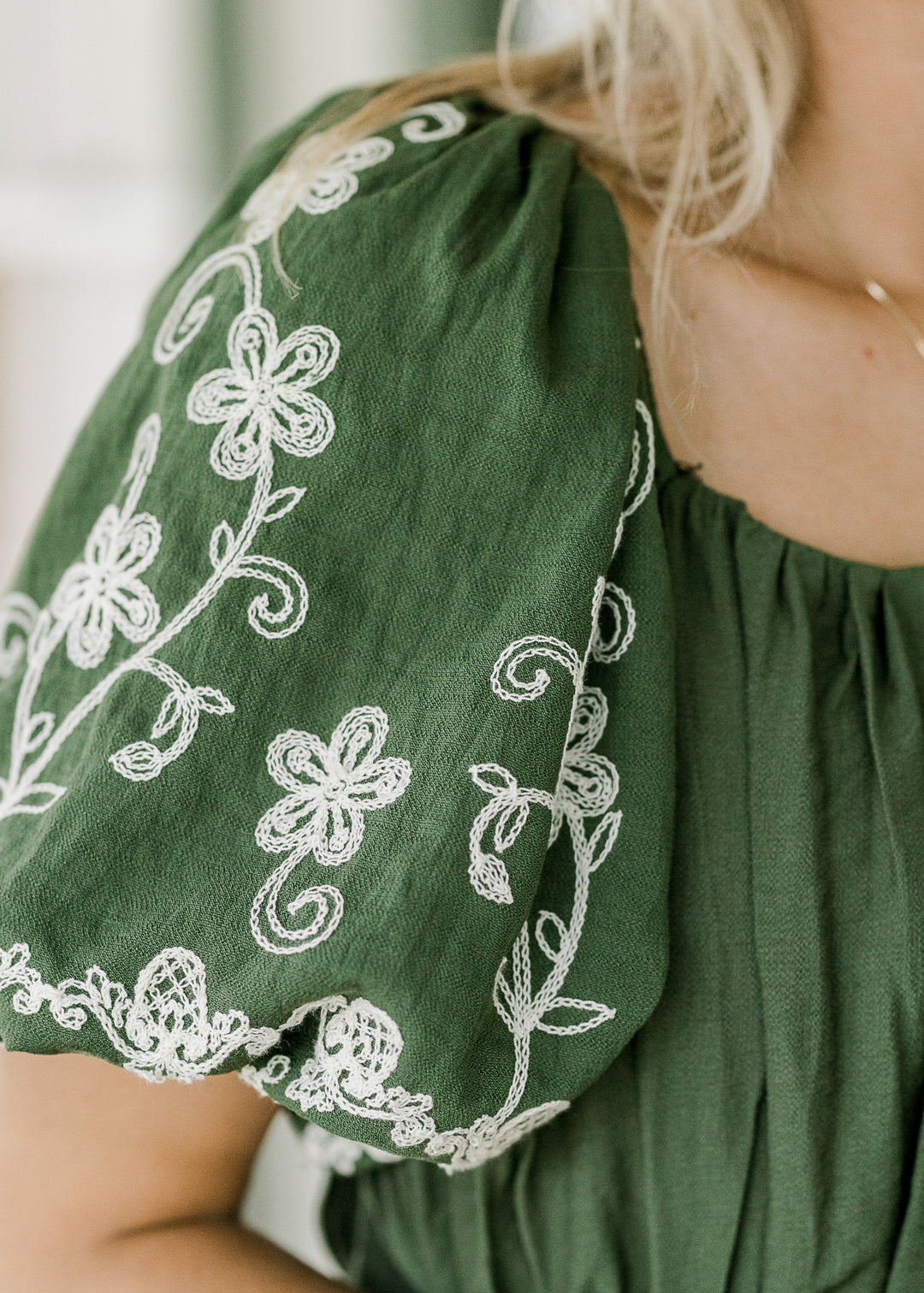 Close up of bubble short sleeves with cream floral embroidery on a hunter green dress. 