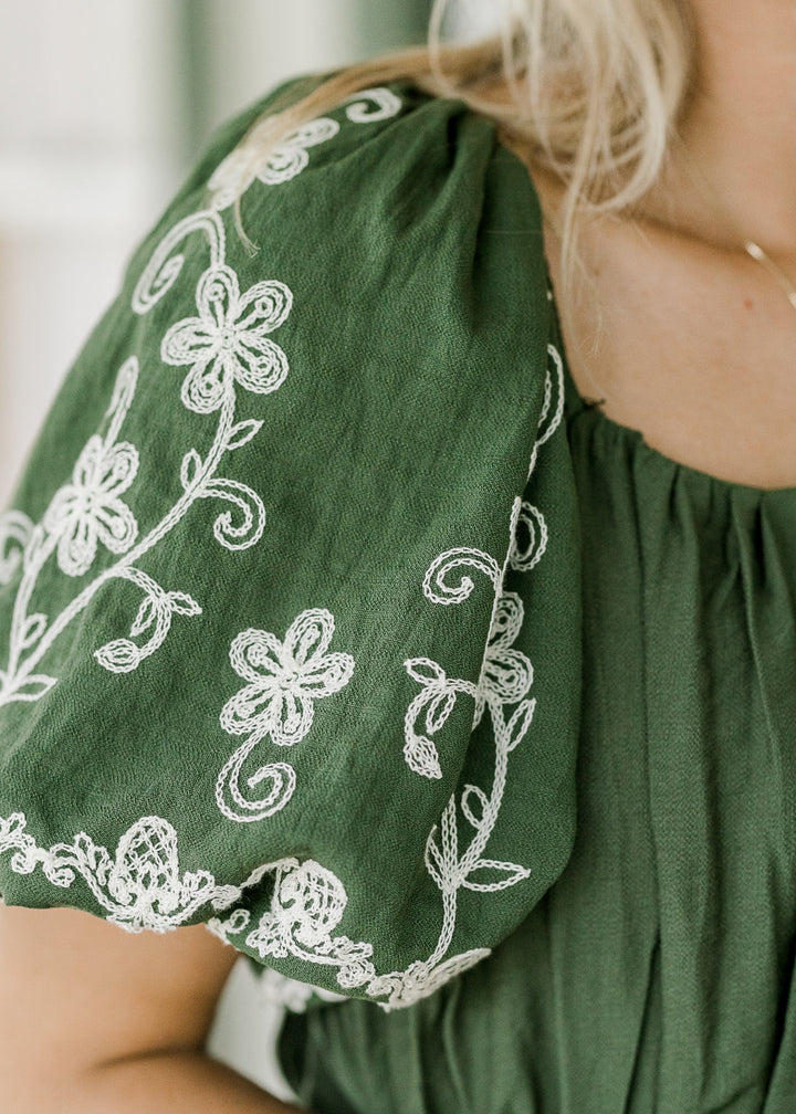 Close up of bubble short sleeves with cream floral embroidery on a hunter green dress. 