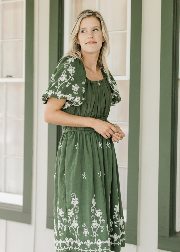 Model wearing a hunter green dress with a square neck, cream floral and bubble short sleeves. 