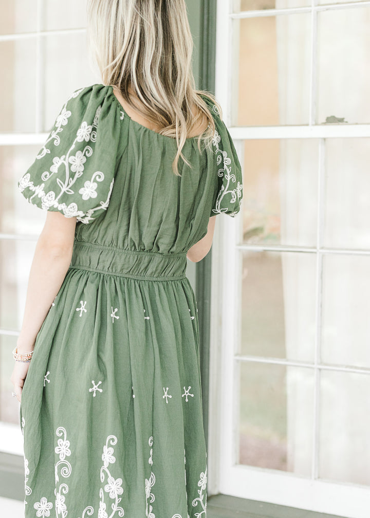 Model wearing a hunter green dress with cream embroidery, elastic waist and bubble short sleeves.