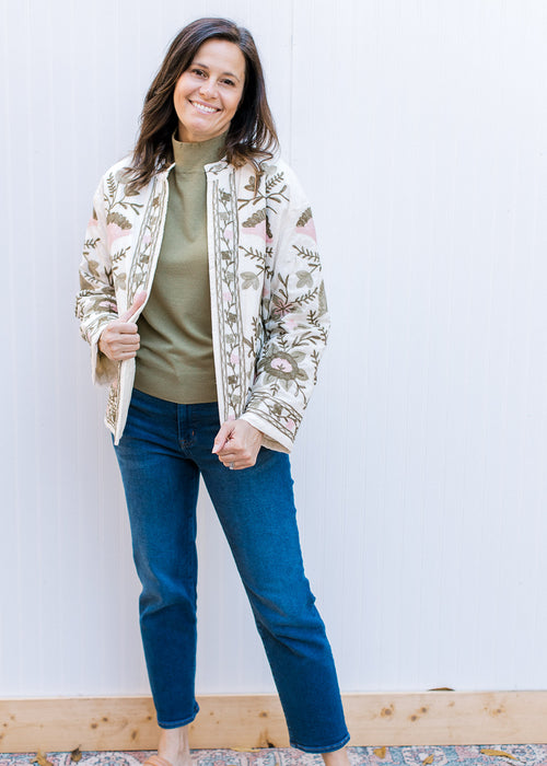 Model wearing a cream open front jacket with pink and green embroidered flowers and long sleeves. 