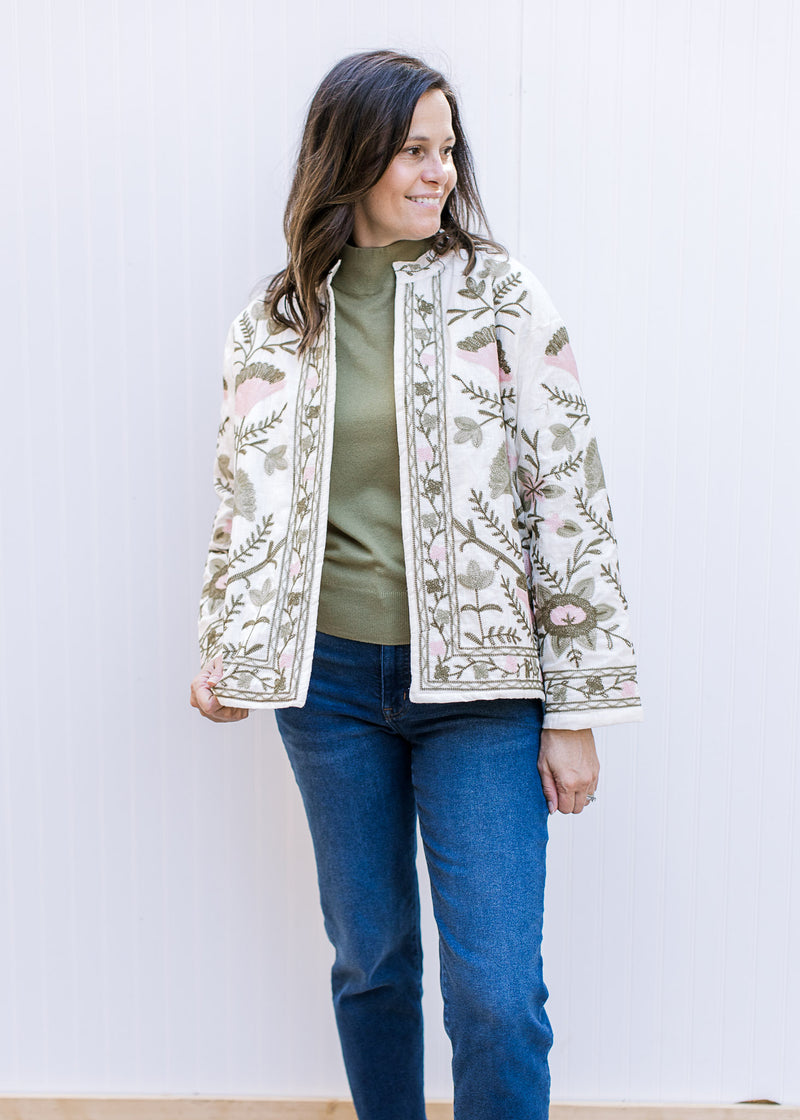 Model wearing a jeans and a cream floral jacket with a long sleeve olive green sweater. 