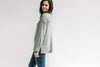 Side view of Model wearing a olive long sleeve sweater with a turtleneck and small side slits. 