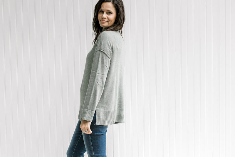 Side view of Model wearing a olive long sleeve sweater with a turtleneck and small side slits. 