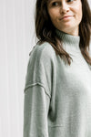 Close up of drop shoulder and turtleneck on a model in an olive colored long sleeve sweater. 
