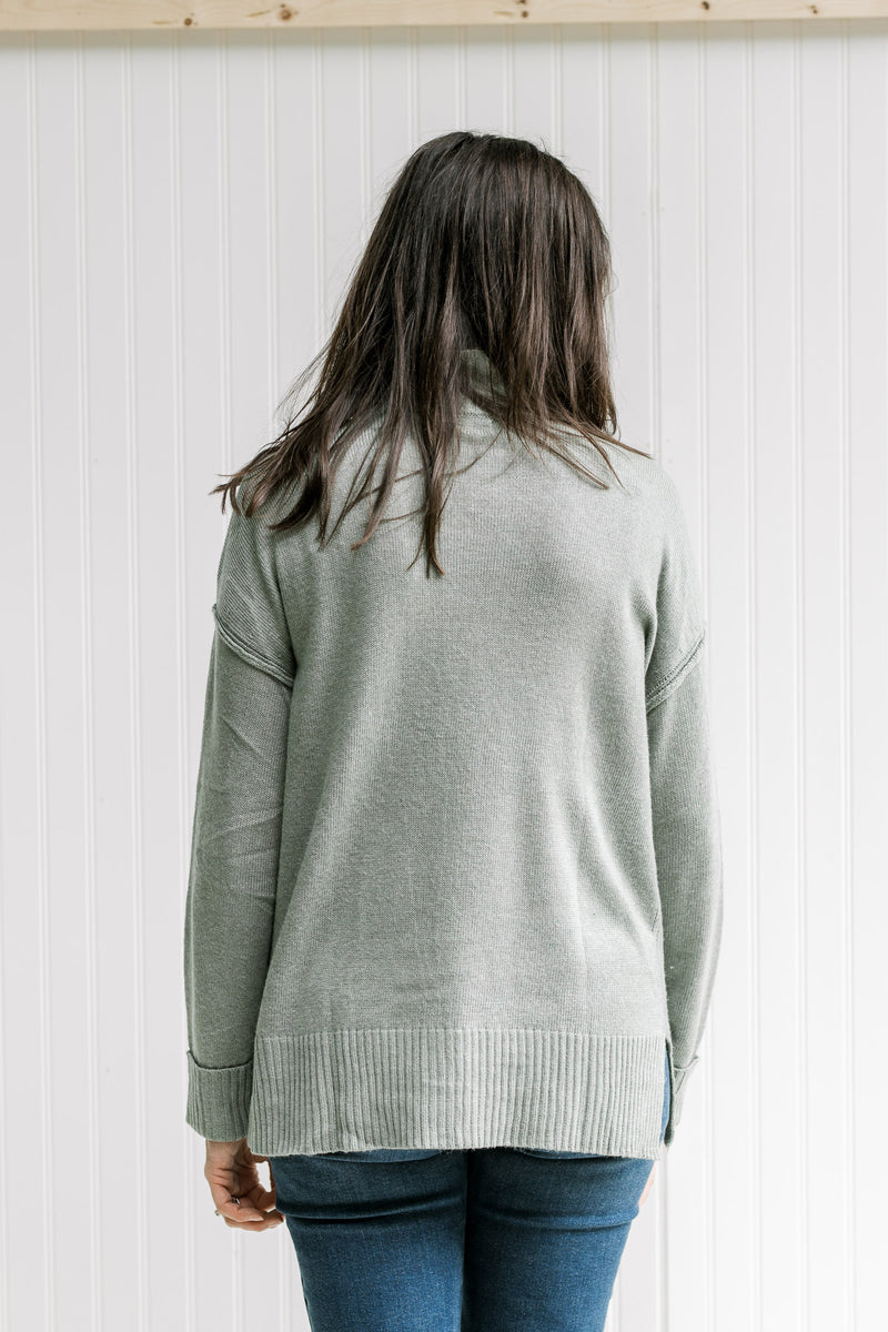Back view of Model wearing an olive long sleeve sweater with drop shoulder and small side slits. 