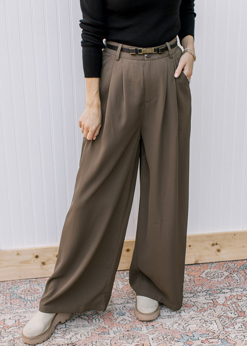 Model wearing warm brown pleated trousers with wide legs and pockets. 