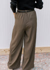 Back view of Model wearing warm brown pleated pants with wide legs and elastic band in back. 