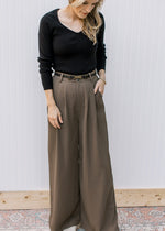 Model wearing a black top with warm brown pleated trousers with wide legs and pockets. 