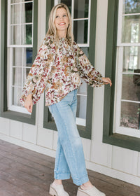 Model wearing jeans, mules and a cream top with warm fall floral, high neck ruffle and long sleeves.